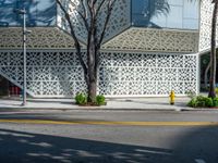 a yellow fire hydrant is in a city street by a building that has white lattices over it