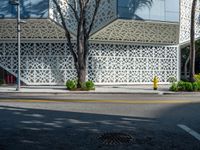 a yellow fire hydrant is in a city street by a building that has white lattices over it