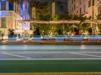 cars passing down a street in front of a large hotel with lots of trees and lamps