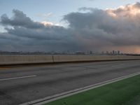 the view of a city from a freeway under cloudy skies at dusk, and a man in white suit stands with his arms crossed