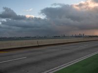 the view of a city from a freeway under cloudy skies at dusk, and a man in white suit stands with his arms crossed