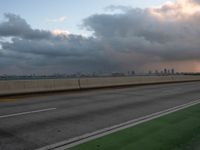 the view of a city from a freeway under cloudy skies at dusk, and a man in white suit stands with his arms crossed