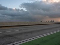 the view of a city from a freeway under cloudy skies at dusk, and a man in white suit stands with his arms crossed