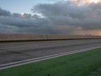 the view of a city from a freeway under cloudy skies at dusk, and a man in white suit stands with his arms crossed