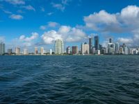 the city skyline is visible from a large body of water in front of it is partly cloudy skies