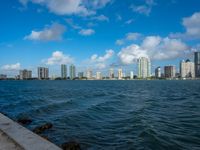 the city skyline is visible from a large body of water in front of it is partly cloudy skies