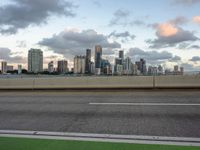 an empty freeway with city in the distance during sunset time against a blue cloudy sky