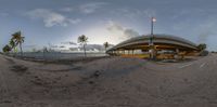 a view of a city from a fish eye lens at sunset with an orange bench on the shore, palm trees and sky behind the river