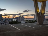 the sun sets behind a large building near the ocean with lots of tall buildings in front