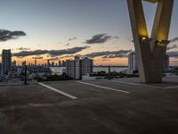 the sun sets behind a large building near the ocean with lots of tall buildings in front