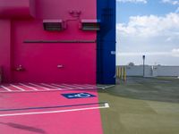 a pink building with blue and yellow paint on the side of it next to a parking lot