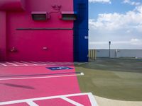 a pink building with blue and yellow paint on the side of it next to a parking lot