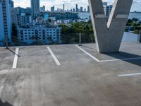 a view of cityscapes in the distance from an empty parking lot, with a person on a skateboard and holding a skateboard