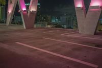 two big pink lights illuminate an empty parking space with city views behind them