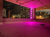 a skateboard sitting under a pink neon sign in a parking garage with tall buildings and lights on it