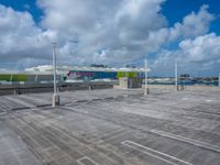 a parking lot is shown with a bus in the background as clouds gather overhead and there are several airport gates