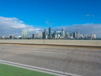 a highway with a green bike path and a cityscape in the distance with a blue sky