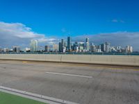 a highway with a green bike path and a cityscape in the distance with a blue sky