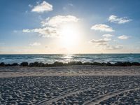 a blue sky filled with clouds, water and sand in front of some rocks and the ocean