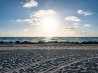 a blue sky filled with clouds, water and sand in front of some rocks and the ocean