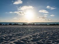 a blue sky filled with clouds, water and sand in front of some rocks and the ocean