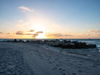 the sun rises over the ocean from an open beach with rocks and surf boards in front