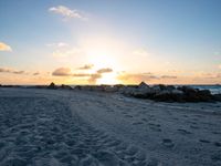 the sun rises over the ocean from an open beach with rocks and surf boards in front