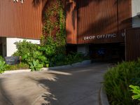 the entrance to an apartment with palms trees and bushes in the foreground, next to a concrete driveway