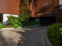 the entrance to an apartment with palms trees and bushes in the foreground, next to a concrete driveway