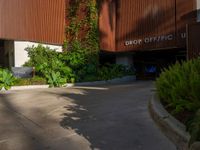 the entrance to an apartment with palms trees and bushes in the foreground, next to a concrete driveway