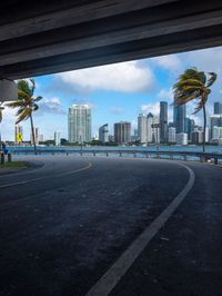 view of downtown miami from beneath highway bridge on a sunny day with palm trees in the distance