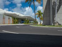 empty road next to large building on sunny day with palm trees in foreground and sky above