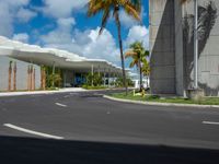 empty road next to large building on sunny day with palm trees in foreground and sky above