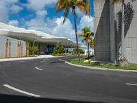 empty road next to large building on sunny day with palm trees in foreground and sky above