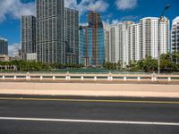 an open road between two large skyscrapers on the water side in a city that has boats and tall buildings