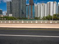 an open road between two large skyscrapers on the water side in a city that has boats and tall buildings