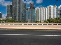 an open road between two large skyscrapers on the water side in a city that has boats and tall buildings