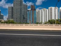 an open road between two large skyscrapers on the water side in a city that has boats and tall buildings