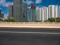 an open road between two large skyscrapers on the water side in a city that has boats and tall buildings