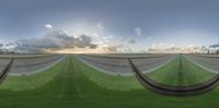 a curved ramp leading into a wide open green field with clouds above it in the sky