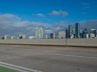 a street view with the city skyline in the distance with clouds overhead on a sunny day