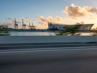 a person on a motorcycle rides along the side of a road in front of a large city with docks