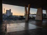 a skateboarder performing tricks in an empty concrete lot with tall buildings in the background