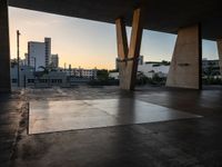 a skateboarder performing tricks in an empty concrete lot with tall buildings in the background