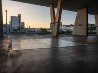 a skateboarder performing tricks in an empty concrete lot with tall buildings in the background