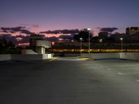 an empty parking lot with a light at the end of it and street lights in the distance