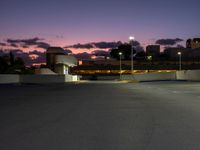 an empty parking lot with a light at the end of it and street lights in the distance