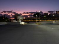 an empty parking lot with a light at the end of it and street lights in the distance