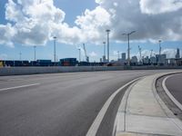 this is an empty highway in an urban setting in the background of city buildings and clouds