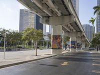 an empty street and buildings with graffiti on it, as pedestrians are walking underneath an elevated rail overpass